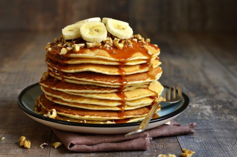 A plate with a large stack of pancakes with bananas on top