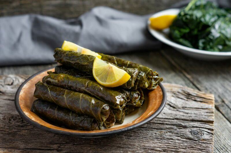 A plate with rolled up collard greens filled with rice or something similar, with a plate of cooked collard greens in the background