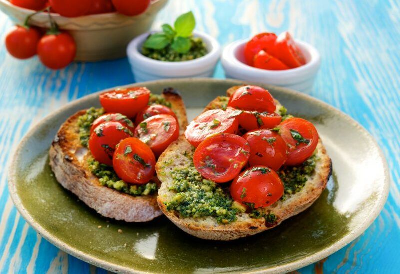 A green plate with two pieces of bruschetta with pesto and sliced tomatoes