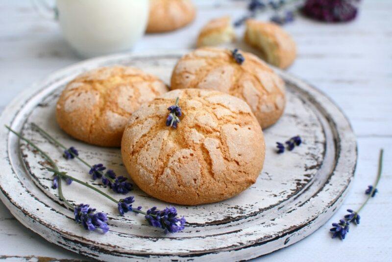 A white plate with three white chocolate lavender cookies, plus some pieces of lavender