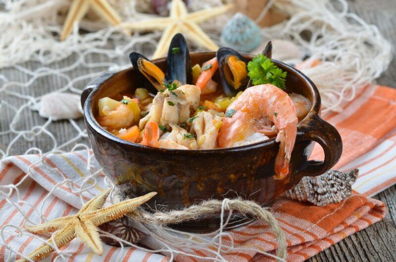 A pot containing a collection of different types of seafood, on a table with netting, starfish, and similar items