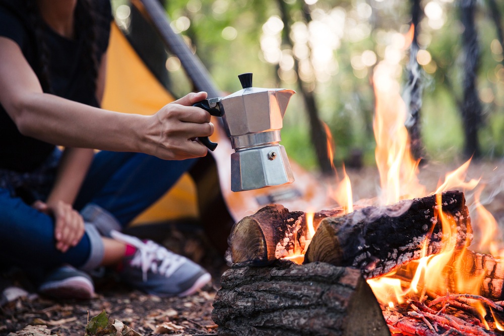 A camper next to a campfire holding a coffee pot