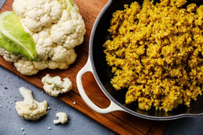 A pot or pan with cooked cauliflower rice and a whole head of cauliflower