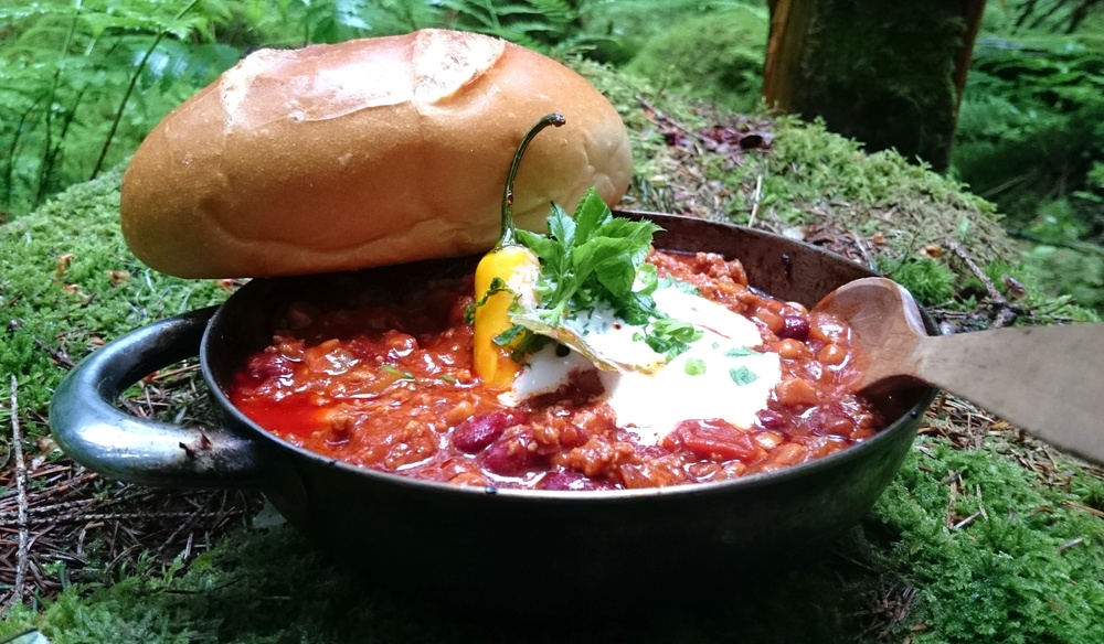 A large pot filled with chilli being cooked outdoors with bread on top