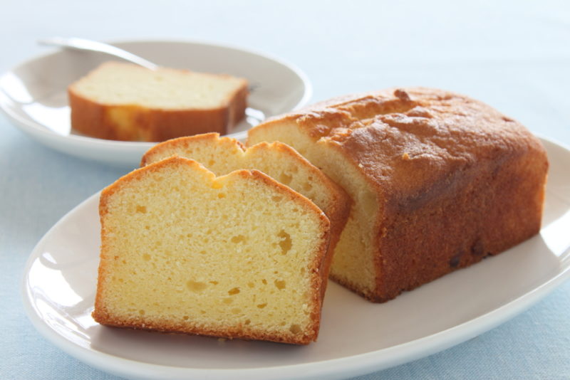 A pound cake on a white plate, with some pieces sliced from it