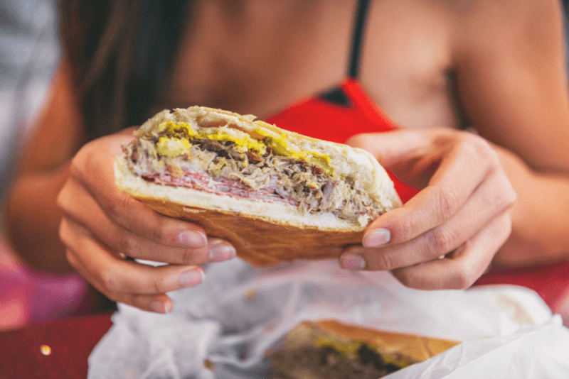 A woman holding a pressed Cubano or Cuban sandwich, where the meat and other fillings can be clearly seen.