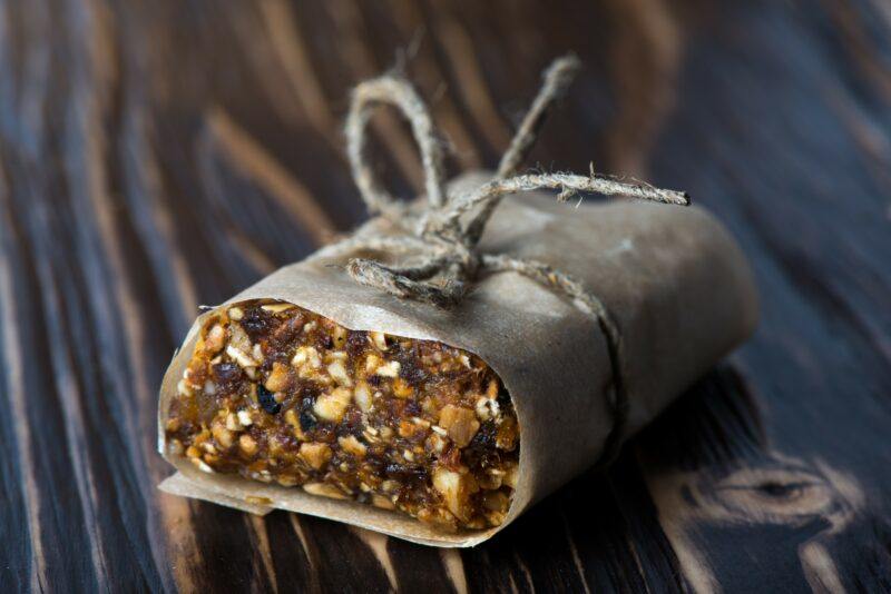 A single protein bar wrapped in paper and tied in a string, on a wooden table