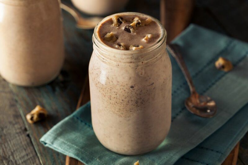 Two glass bottles containing a chocolate protein shake. One is on a blue cloth of some kind.