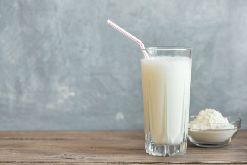 A glass with a vanilla protein shake and a straw, along with a small container of vanilla protein powder