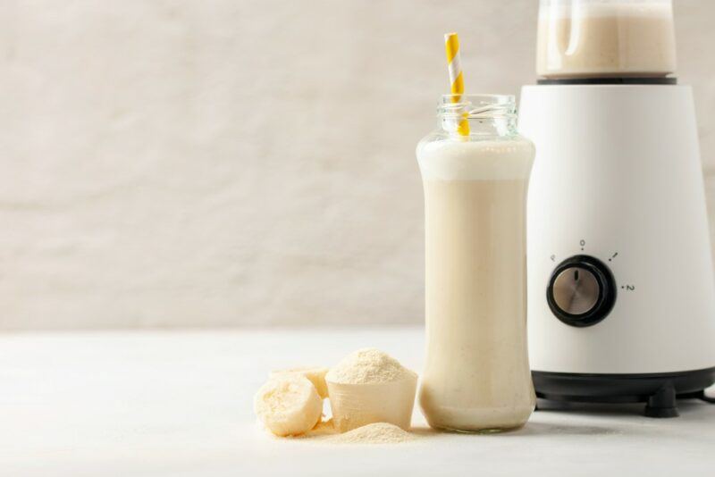 A bottle of vanilla protein shake, next to a blender and some vanilla protein powder