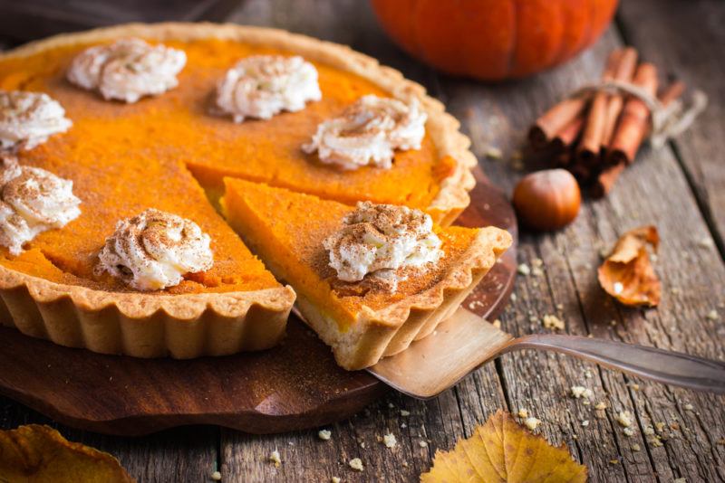 A pumpkin pie on a wooden table with a piece partly cut out of it