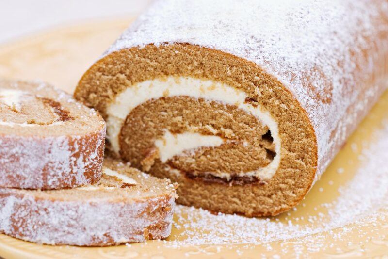 A pumpkin roll cake with two slices cut from it, where the cream cheese filling can be clearly seen