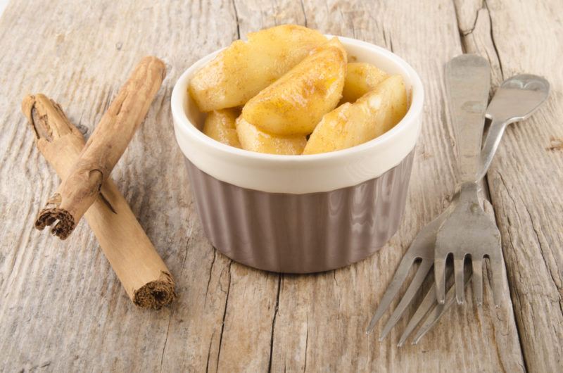 A small container with stewed apples, next to some forks and cinnamon sticks