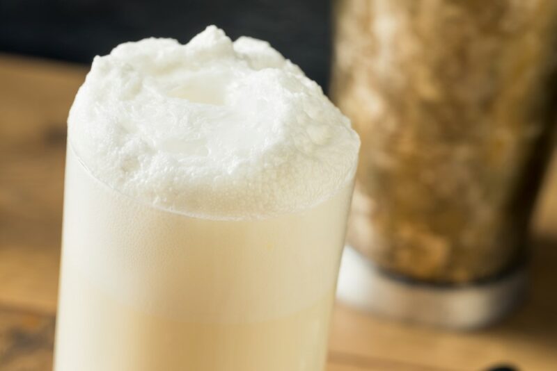 A ramos gin fizz cocktail on a table in front of a cocktail shaker