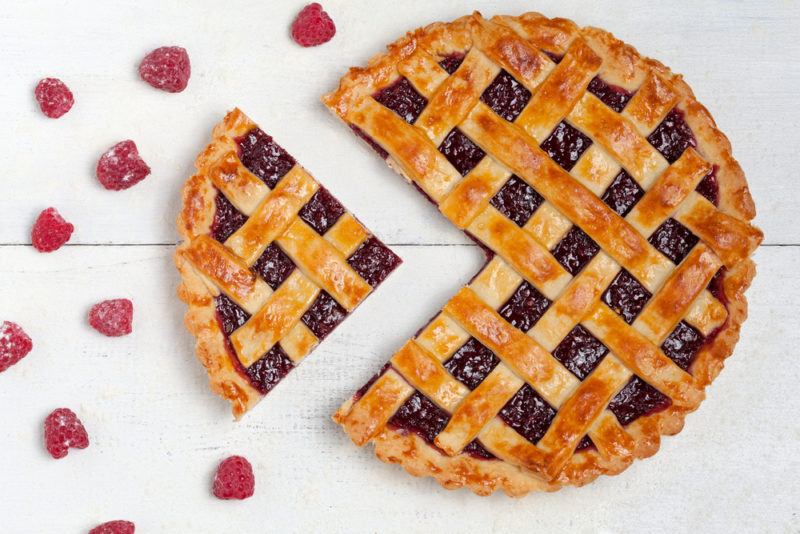 A raspberry and lemon pie with one piece that has been cut out of it and raspberries scattered around