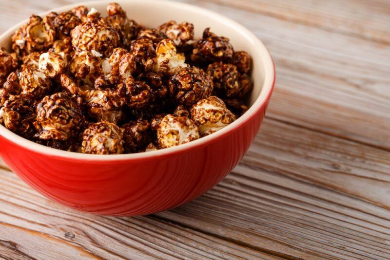 A red and white bowl on a wooden table containing chocolate bacon popcorn