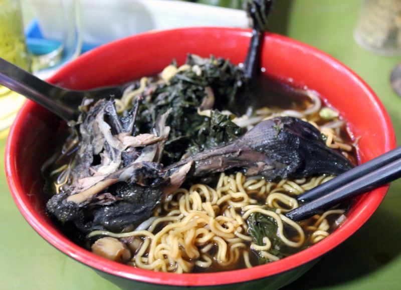 A red bowl that includes dark chicken meat, noodles, and broth