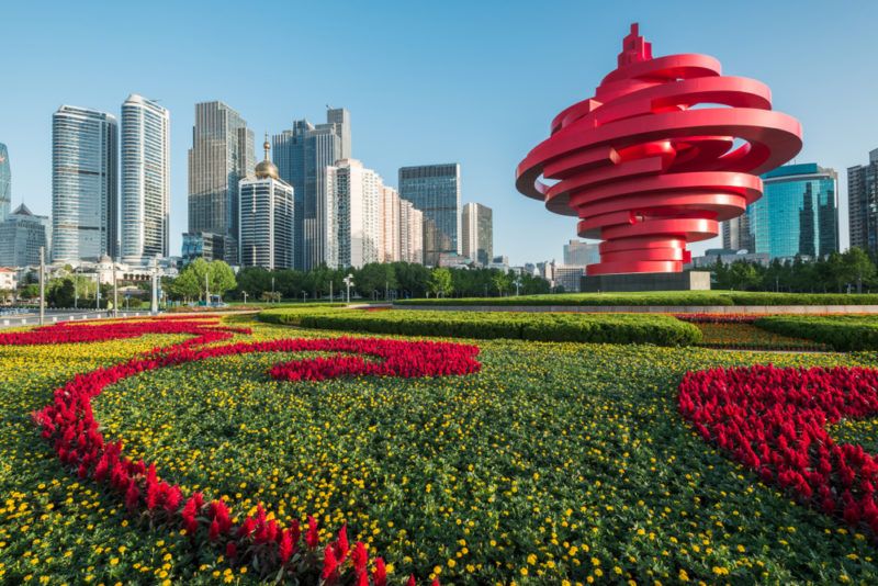 A red building and regular buildings in Shandong China  with red and green grass in front of it