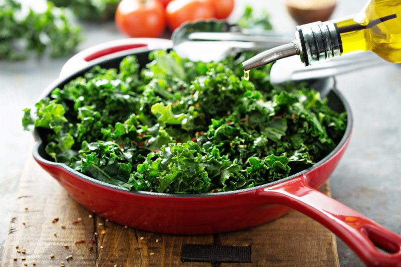 A red frypan with kale that olive oil is being poured into