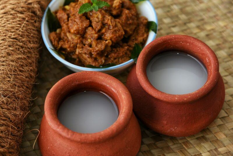 Two terracotta mugs with white Indian toddy, in front of a white bowl of curry