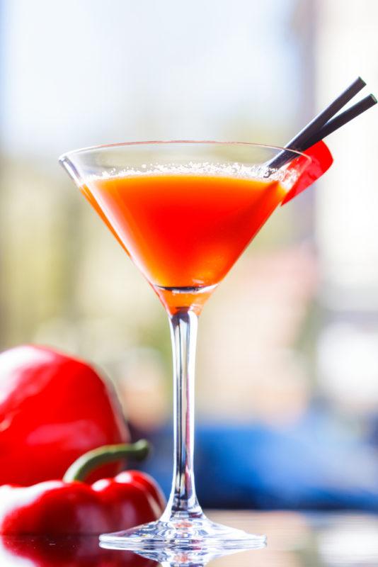 A red pepper martini in a cocktail glass with a red pepper in the background