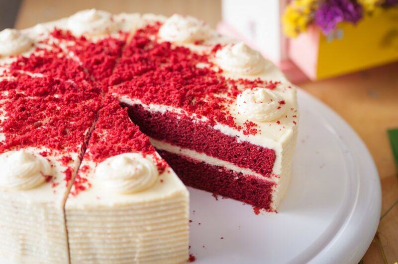 A large red velvet cake with one piece cut out of it, so you can see the cream cheese layers