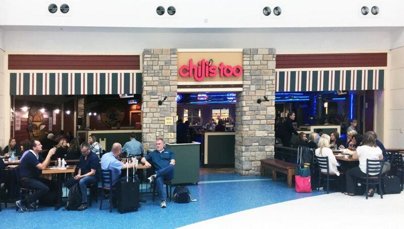 A restaurant called Chiles Too at an airport with many people sitting in front of it