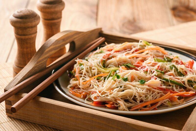 A wooden breakfast tray with a rice noodle dish and some cutlery