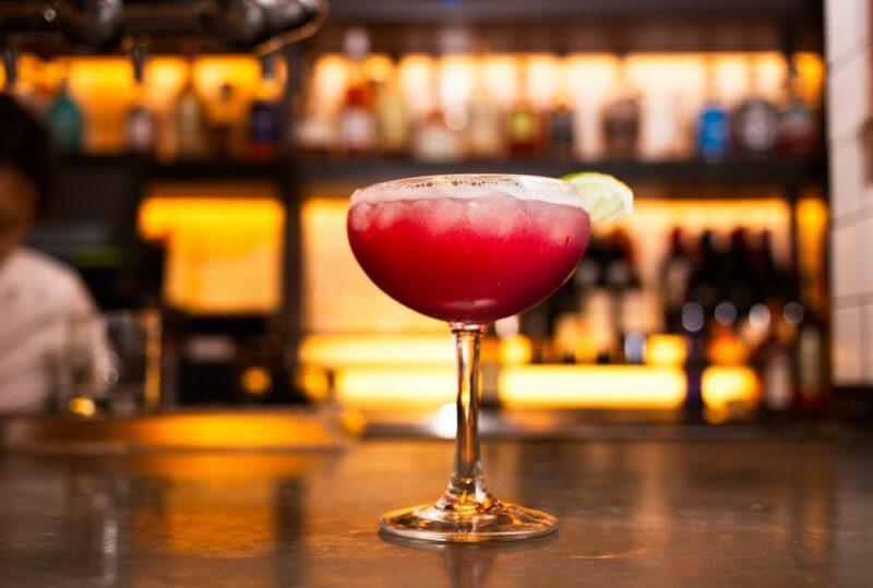 A coupe glass containing a roasted cherry colada cocktail in front of a bar