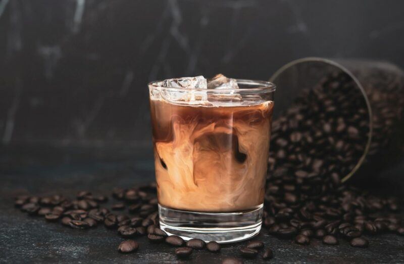 A glass containing a root beer rum cream cocktail next to many coffee beans