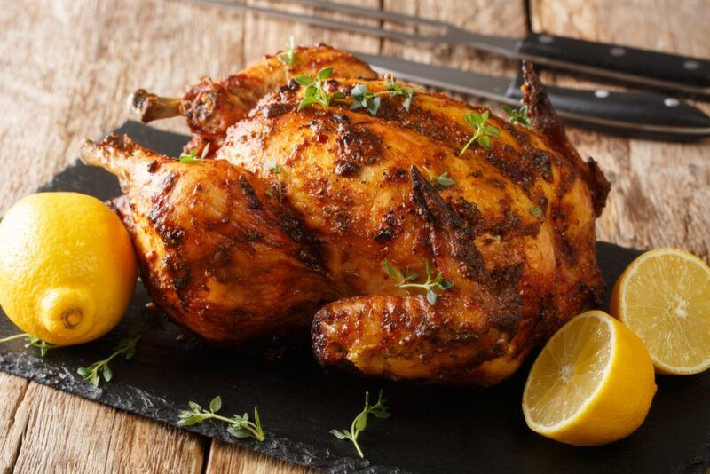 A rotisserie chicken on a blackboard, next to one whole lemon and two lemon halves