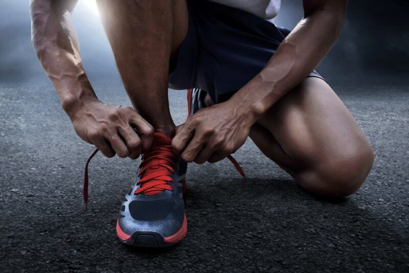 A man crouching down to tie a running shoe with red shoe laces