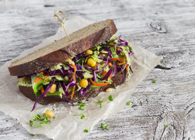 A coleslaw filled rye bread sandwich on white paper