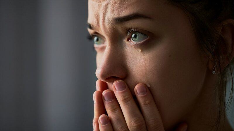 A close image of a sad young woman who has been crying and has her hands over her mouth