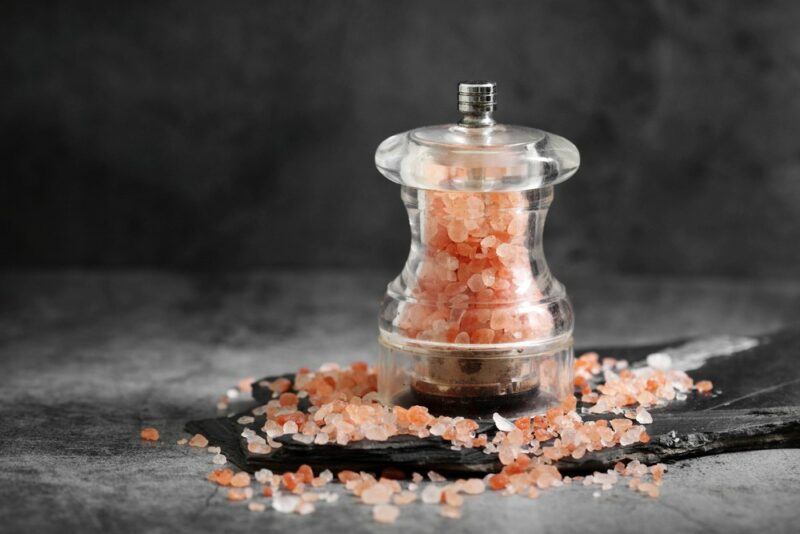 A salt grinder with Himalayan salt on a table, with more salt scattered around