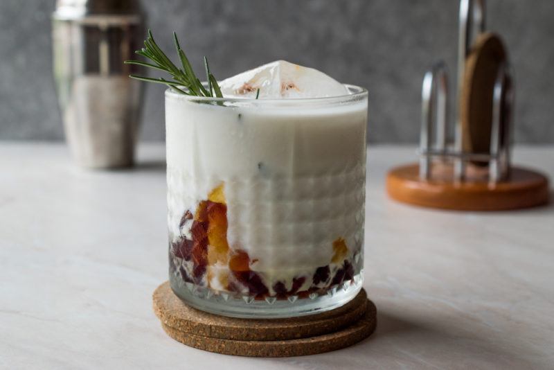 A glass filled with a salted caramel white Russian that has a sprig of rosemary sticking out of it