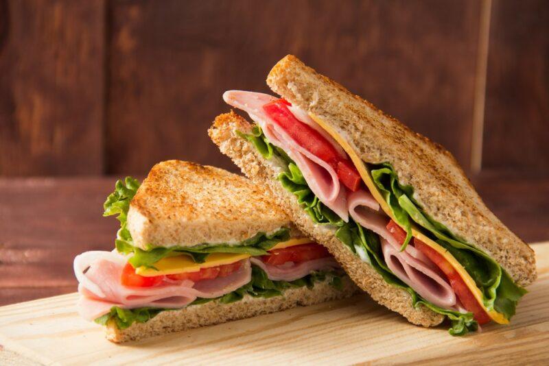 Two halves of a sandwich made using lettuce, tomatoes, cheese, and ham