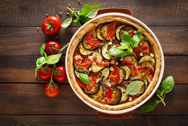 A vegetable tart in a dish on a wooden table next to some tomatoes