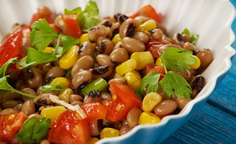 A blue and white scalloped dish with cooked black eyed peas, corn, and tomatoes