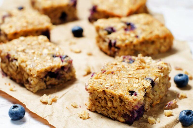 A selection of breakfast bars on a wooden board, with blueberries scattered around