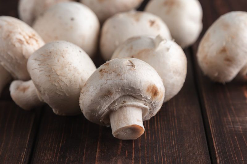 Various clean button mushrooms on a dark wooden table