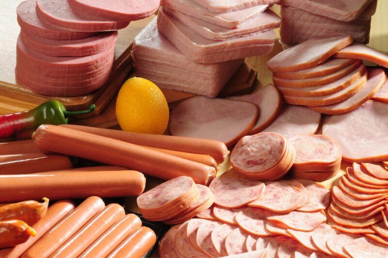 A large collection of cold cut meats and sausages, plus a lemon and a chili pepper.