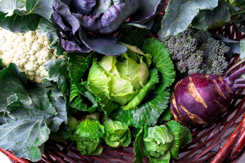 A red basket filled with cruciferous vegetables, including cauliflower and cabbage