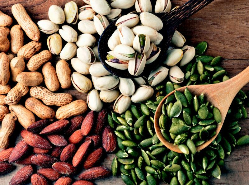 A selection of different nuts and seeds on a table with spoons