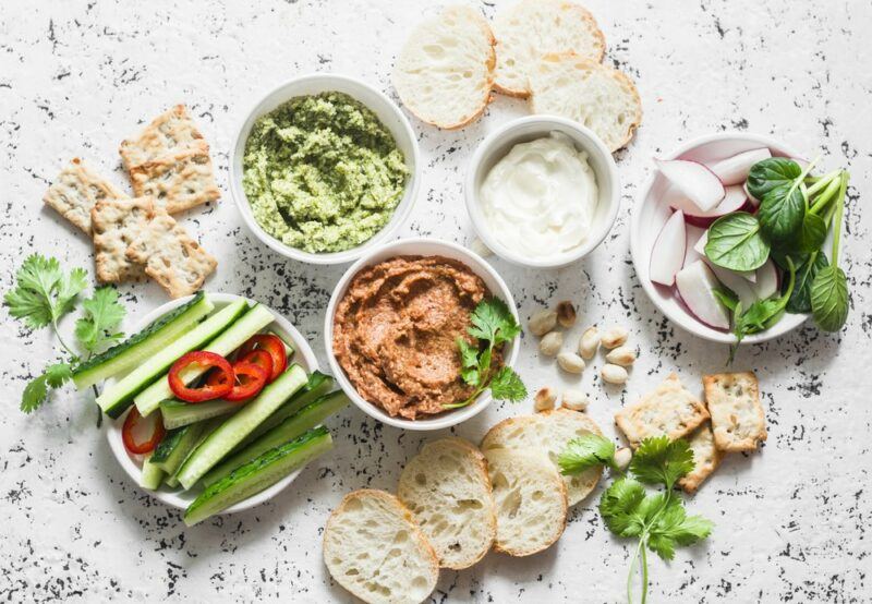 A white table with a selection of different dips and spreads, plus bread and fresh veggies