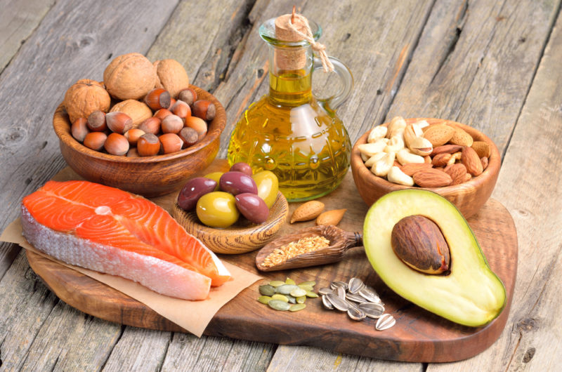 A wooden board containing various healthy fat foods with salmon and avocados