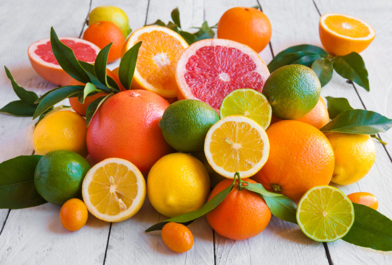 A selection of fresh citrus fruit on a white wooden table with grapefruit, lemons, and limes