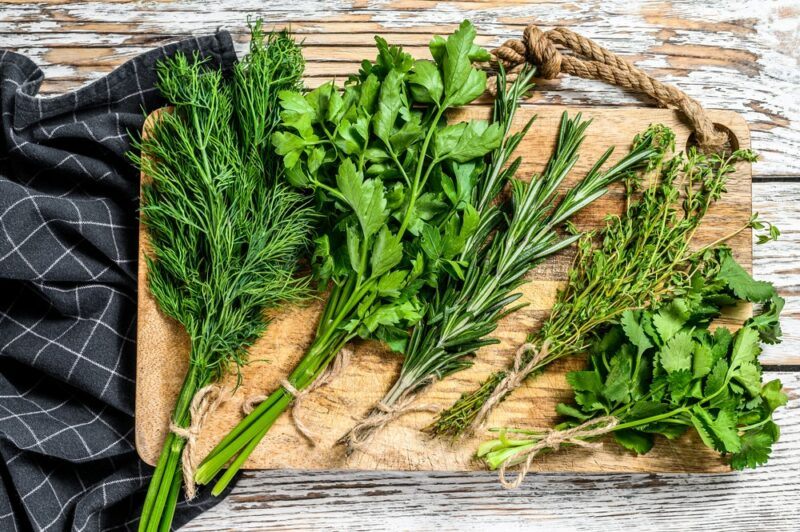 A wooden tray with bunches of fresh herbs on a wooden table