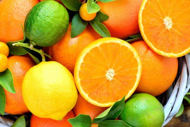 A collection of fresh oranges, a lemon, two limes, and some smaller citrus fruits. There are also two orange slices on top of the other citrus fruits.