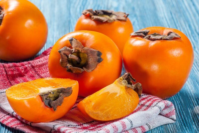 A blue table with a red and white cloth and plenty of fresh persimmons